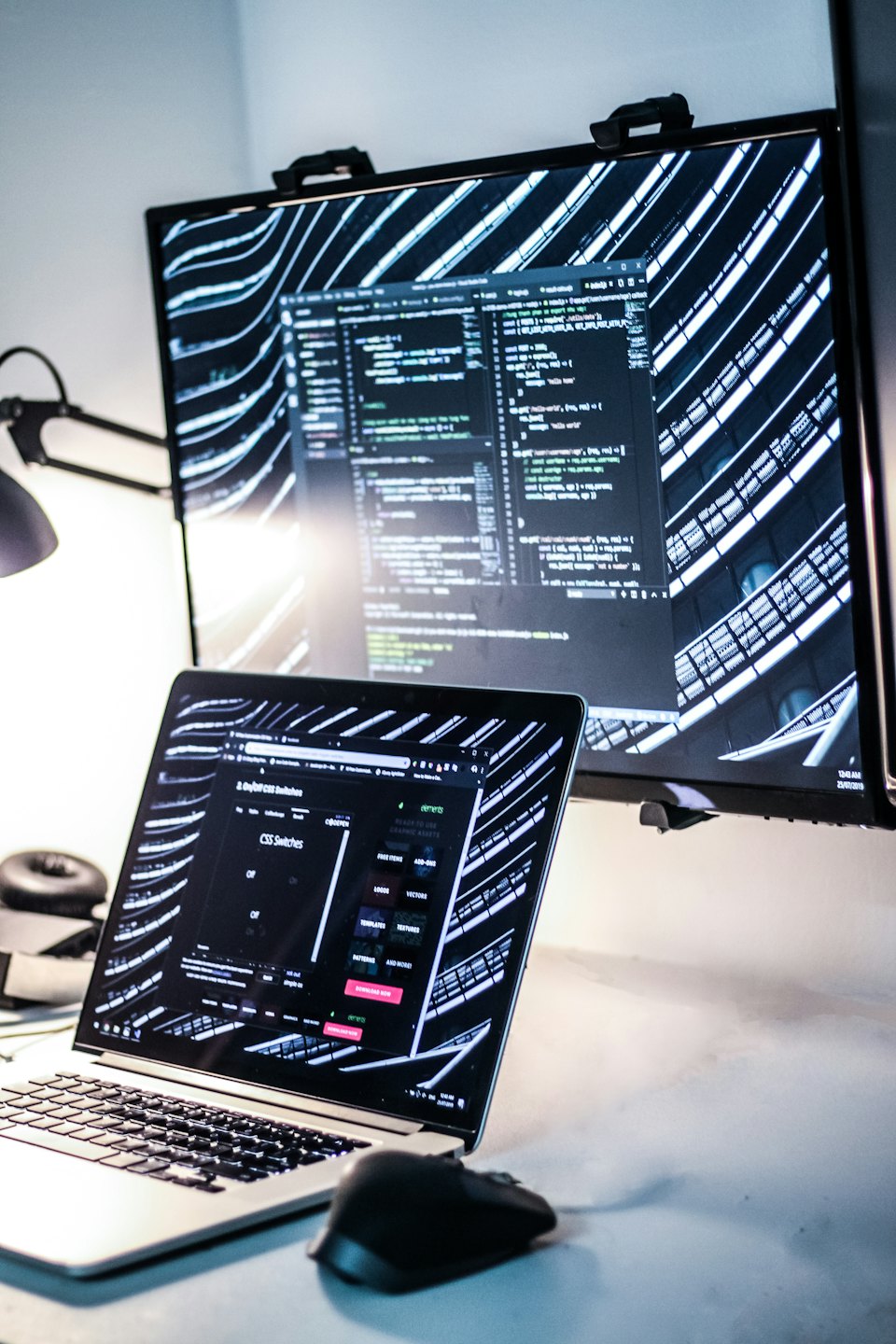 Laptop e monitor che mostrano codice in un ufficio moderno.