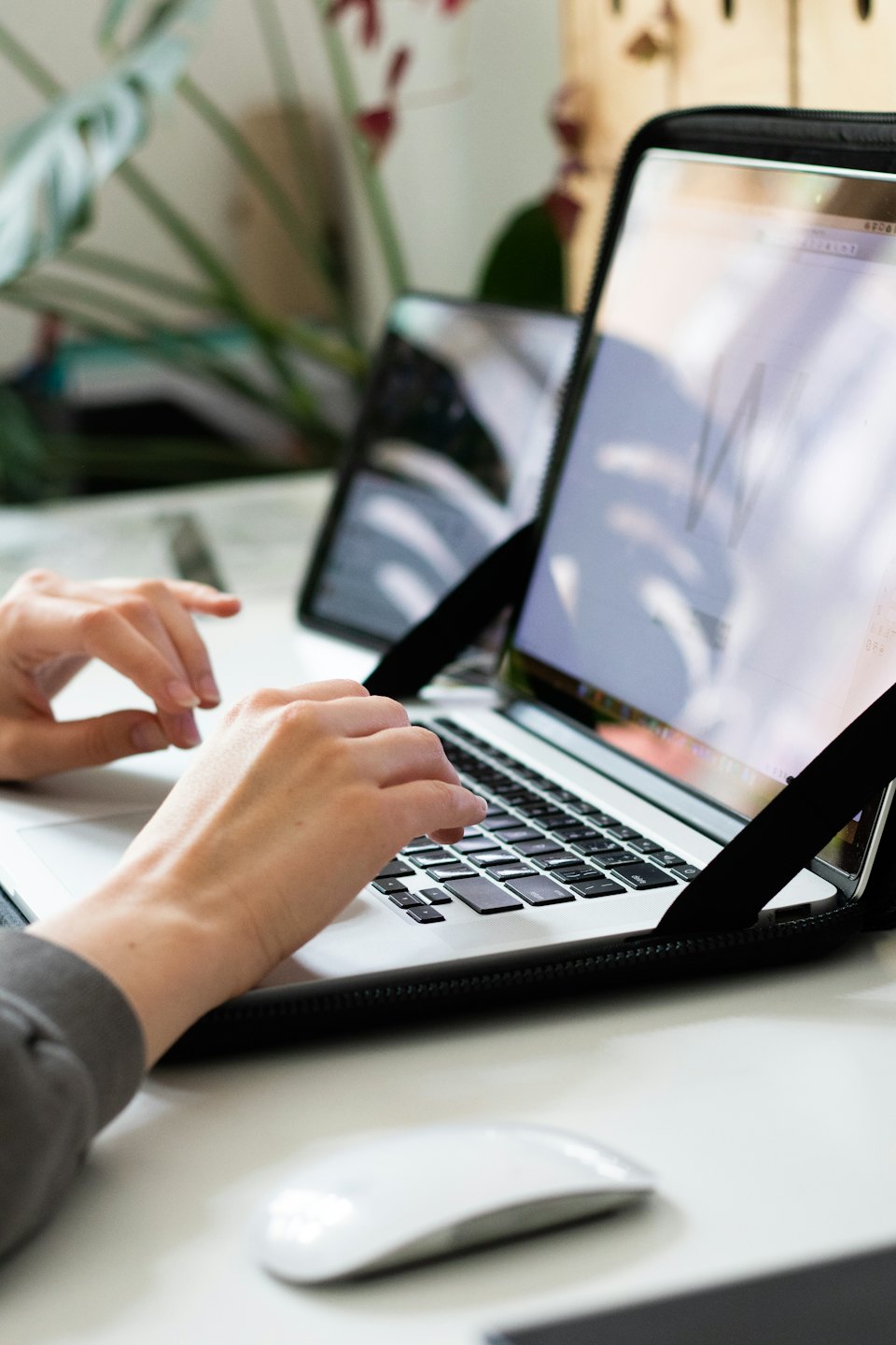 Mani che digitano su una tastiera di un laptop argentato con un mouse.